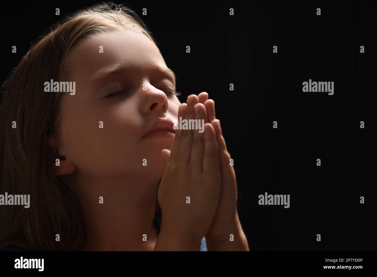 Cute little girl with hands clasped together praying on black ...