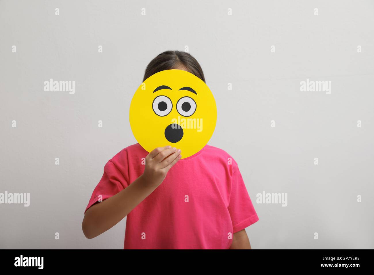Little girl covering face with shocked emoji on white background Stock