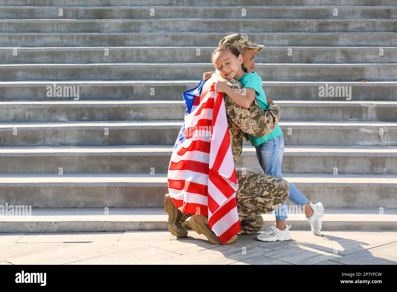 Soldier with flag of USA and his little daughter hugging outdoors, space for text Stock Photo