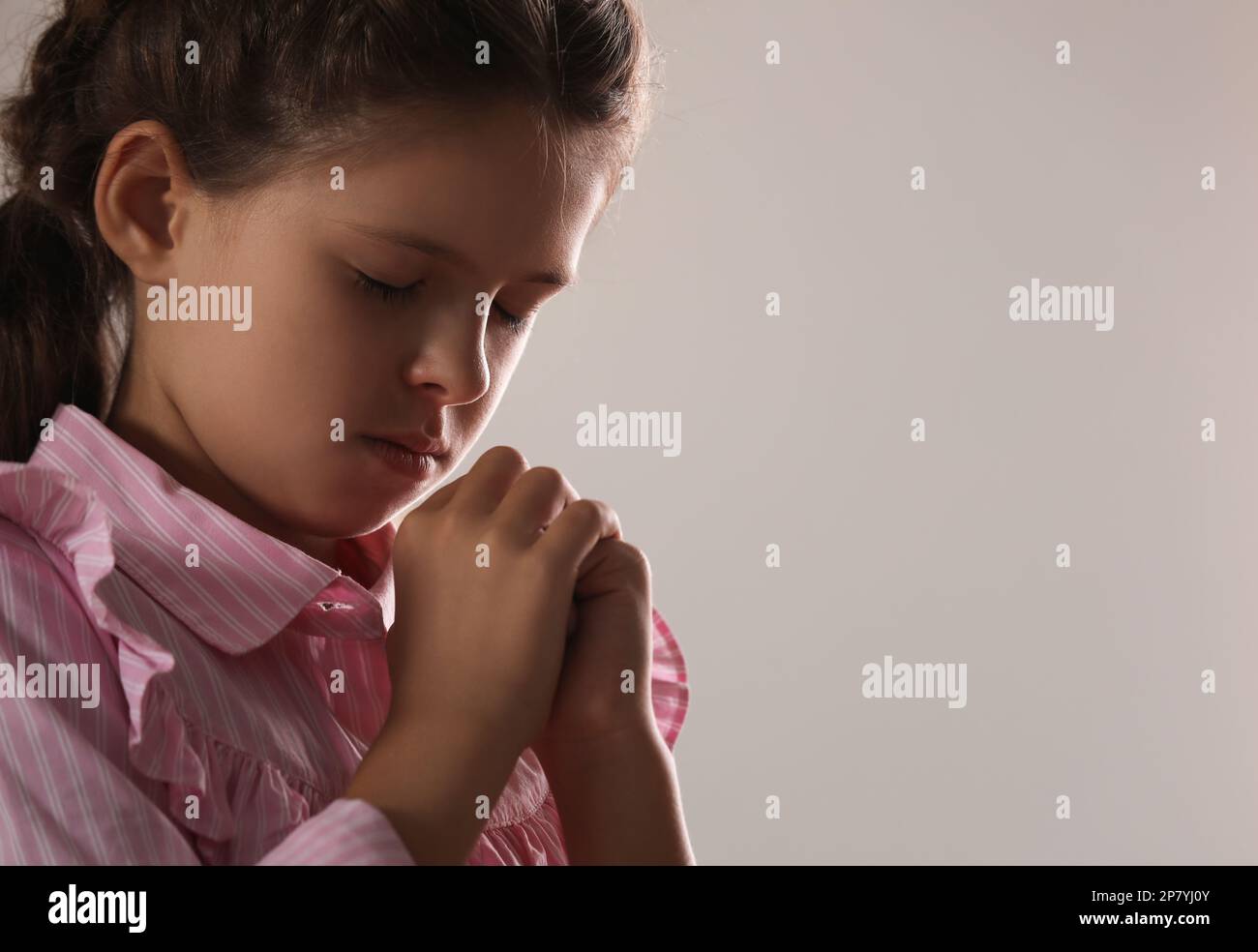 Cute little girl with hands clasped together praying on grey background ...