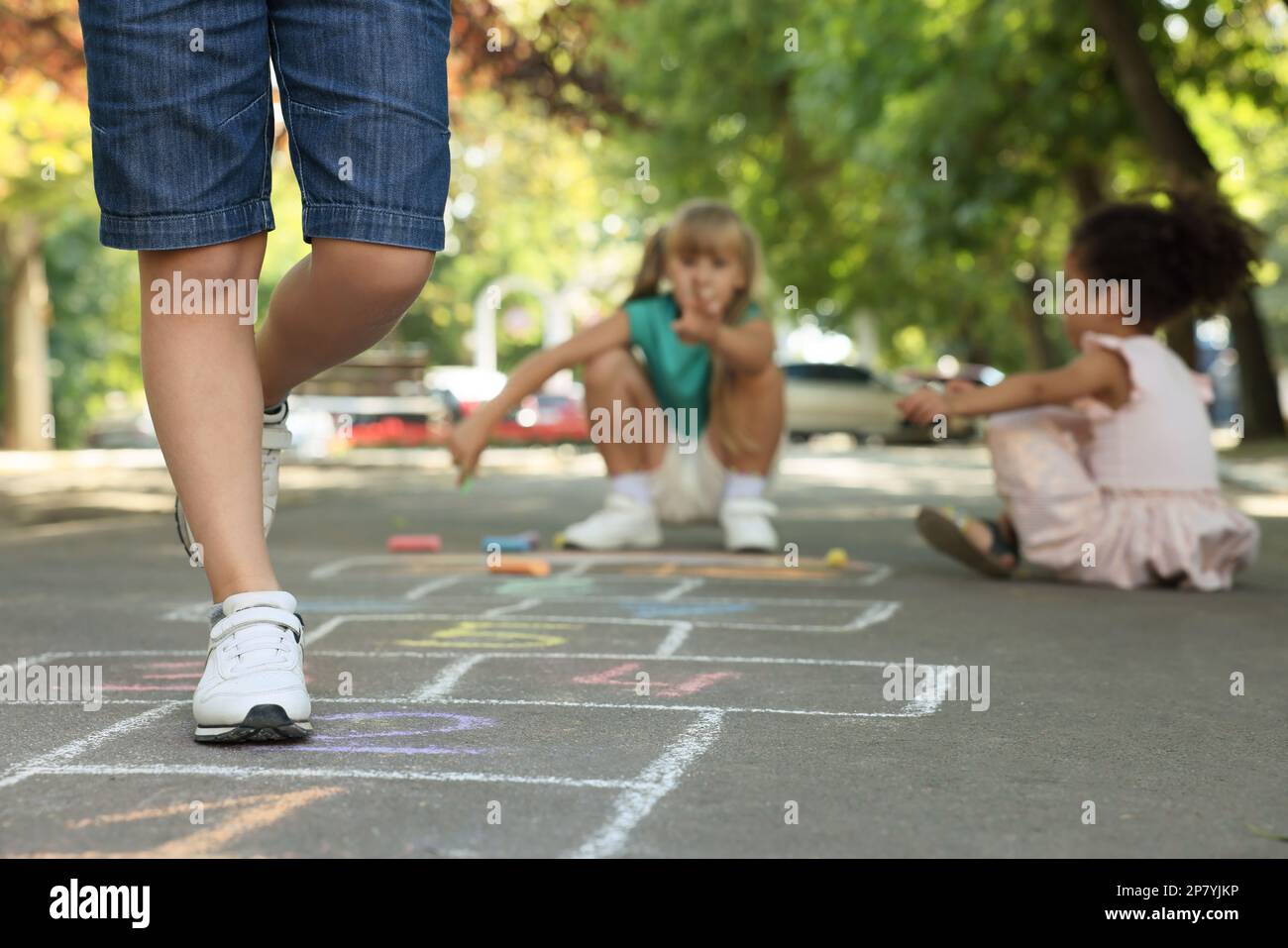 Little children playing hopscotch drawn with chalk on asphalt outdoors ...