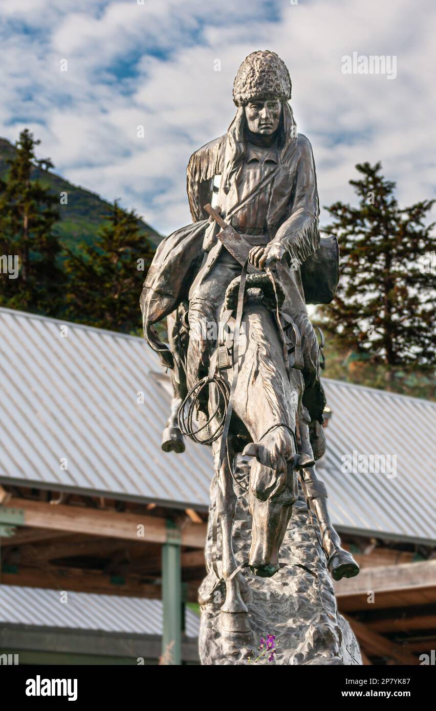 Girdwood, Alaska, USA - July 23, 2011: Equestrian statue of jumping horse with Russian-themed, packed male trader. Green foliage, gray metal sheet bac Stock Photo