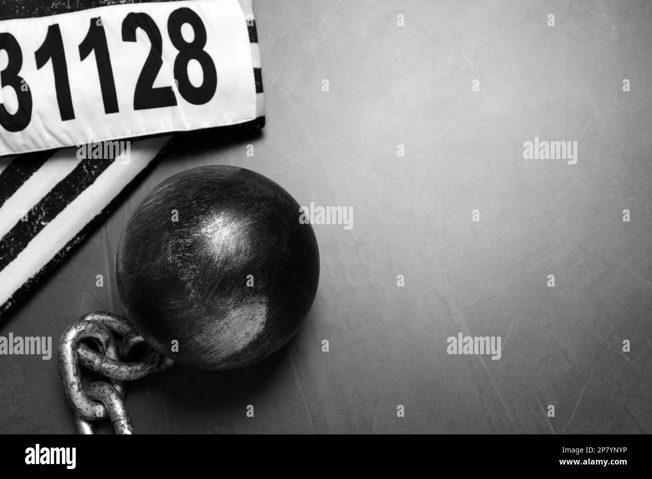 Prisoner ball with chain and jail clothes on grey table, flat lay