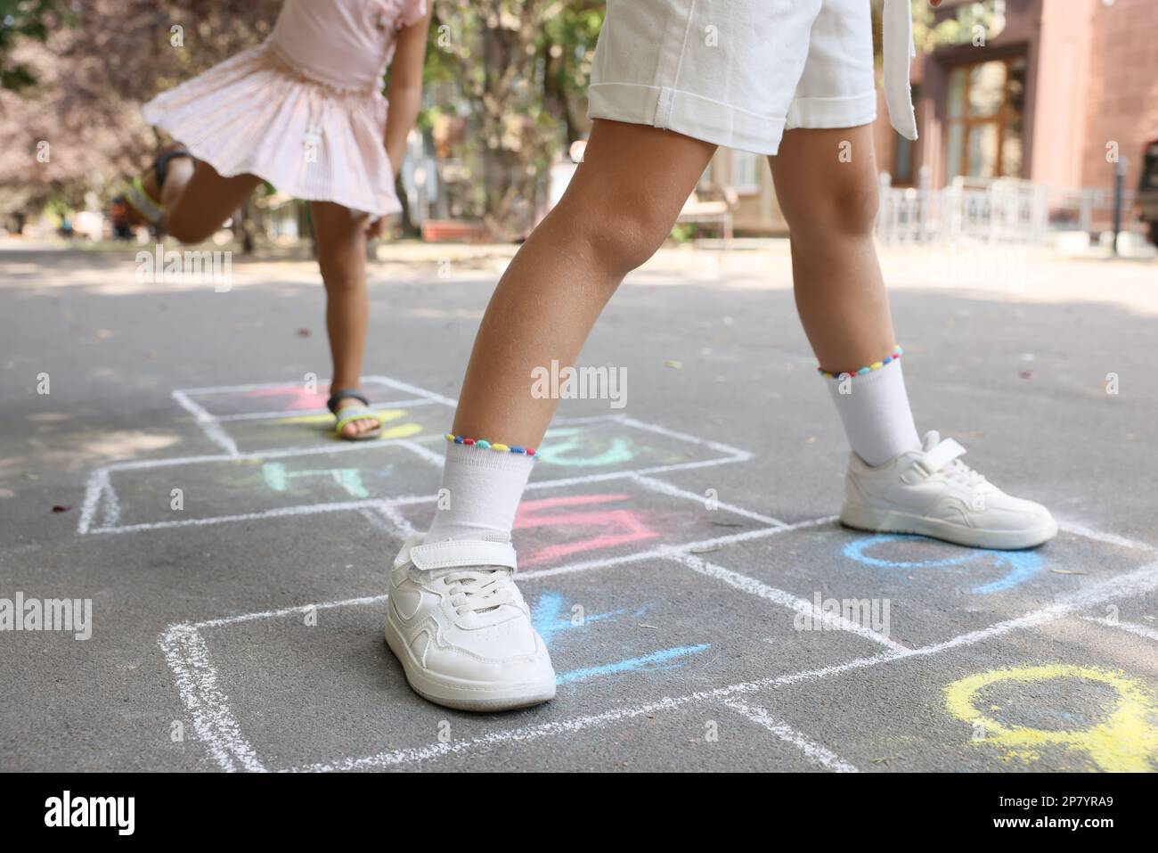 Little children playing hopscotch drawn with chalk on asphalt outdoors, closeup Stock Photo