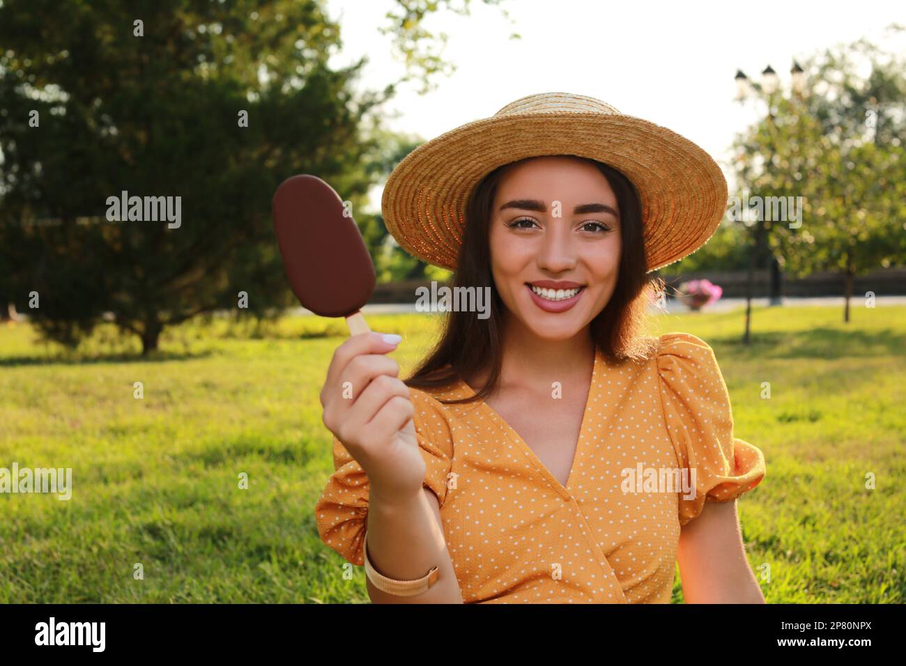 Beautiful young woman holding ice cream glazed in chocolate outdoors Stock Photo