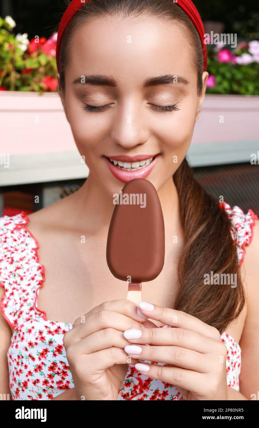Beautiful young woman eating ice cream glazed in chocolate outdoors Stock Photo