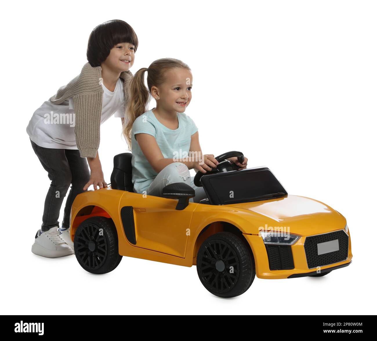 Cute boy pushing children's electric toy car with little girl on white