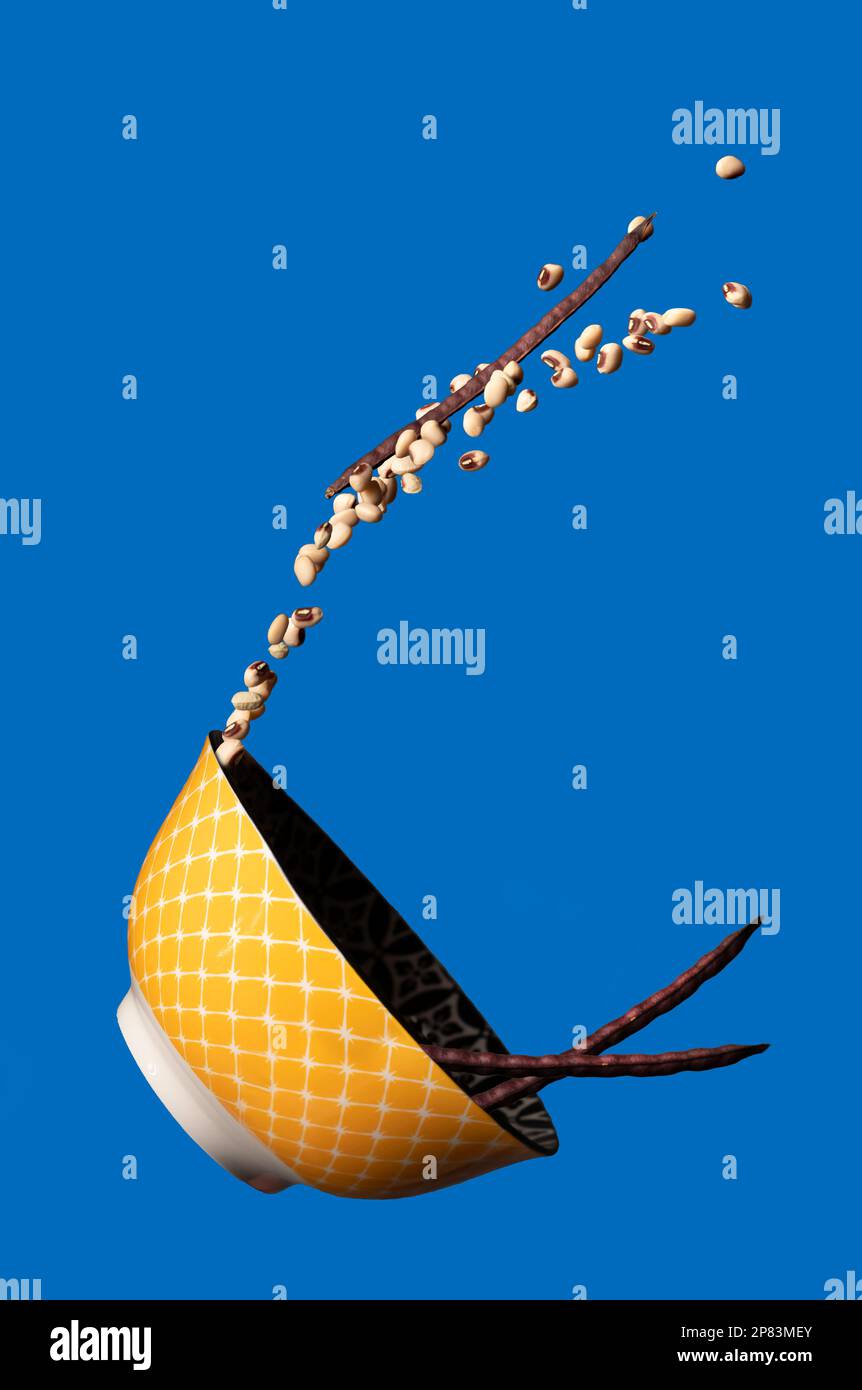 Fun image of a tossed ceramic bowl on a blue background in mid-air spilling black-eyed peas. Stock Photo