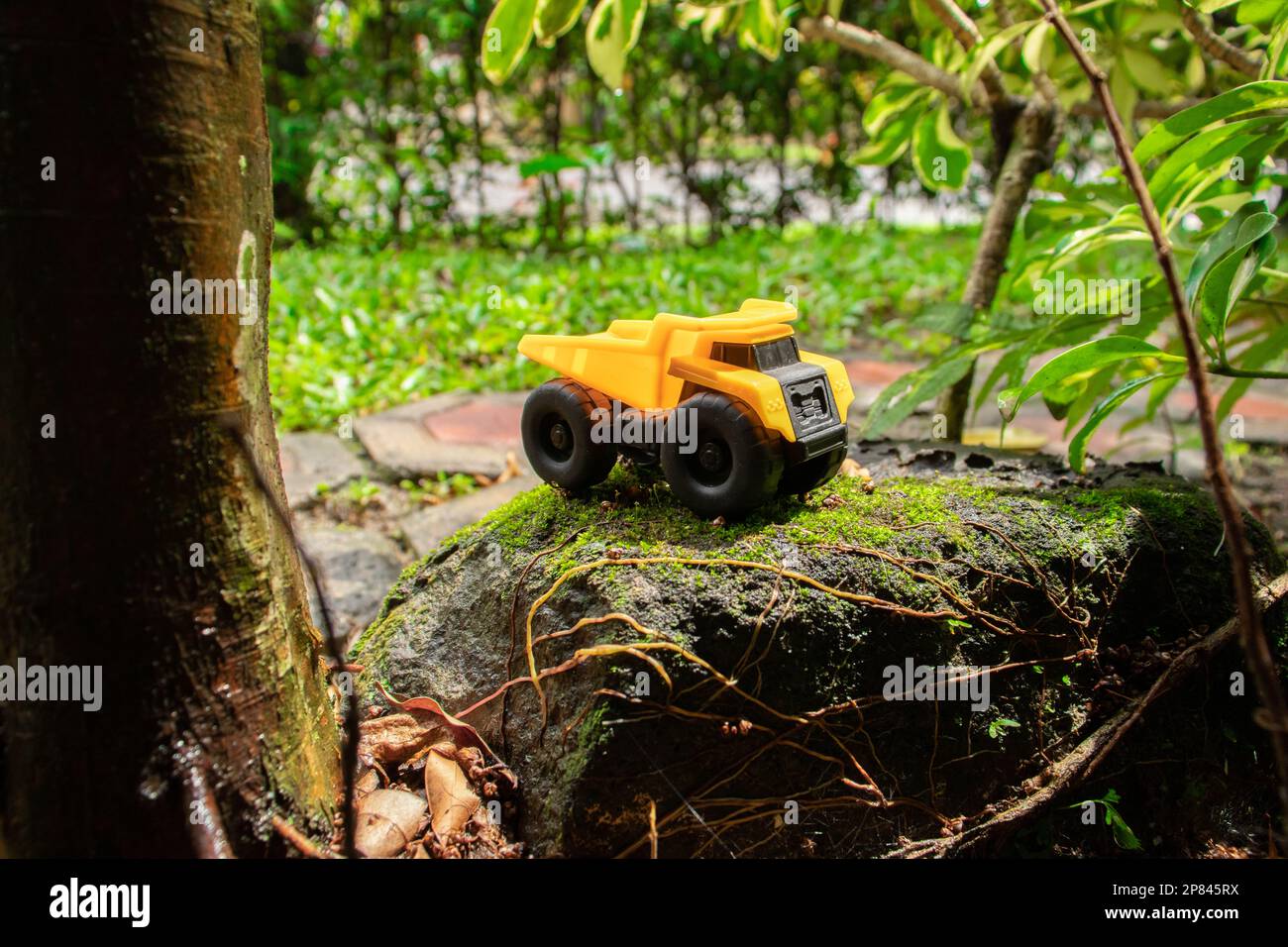 A photo after some edits. A yellow dump truck on a mossy stone. Stock Photo