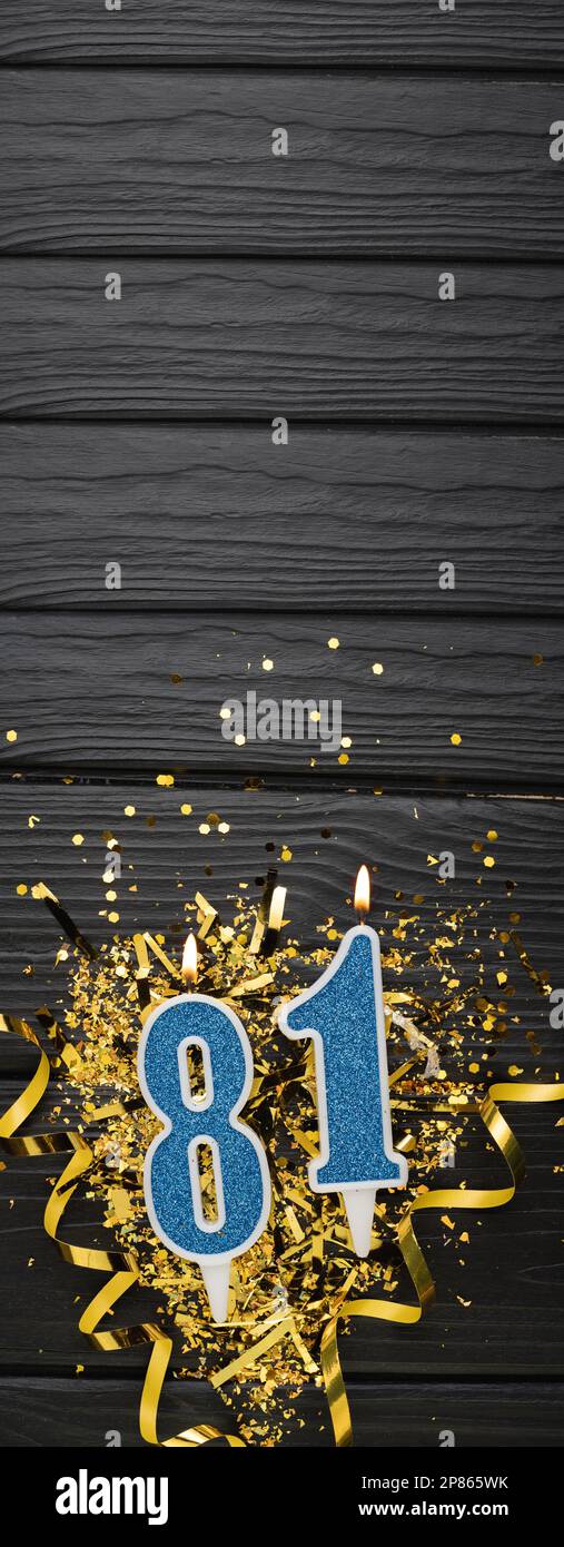 Number 81 blue celebration candle and gold confetti on dark wooden background. 81th birthday card. Anniversary and birthday concept. Vertical banner. Stock Photo