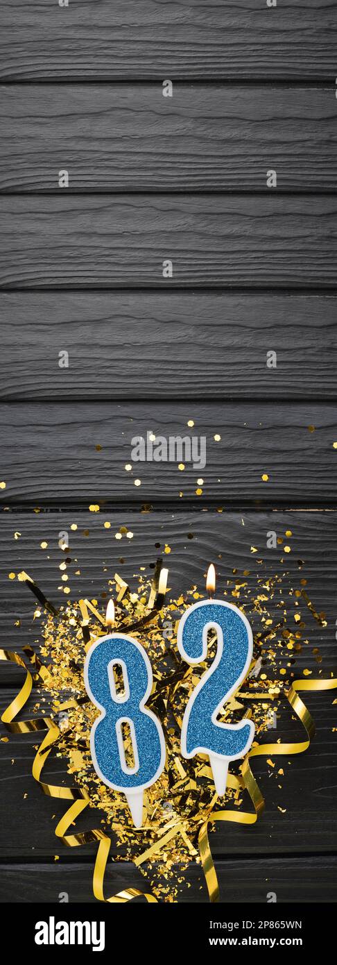 Number 82 blue celebration candle and gold confetti on dark wooden
