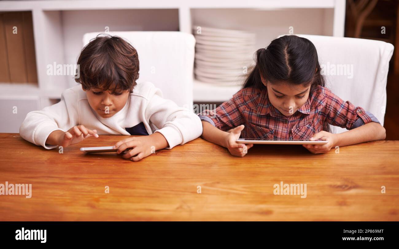 They each have their own tech toy. two siblings playing with their digital devices at home. Stock Photo