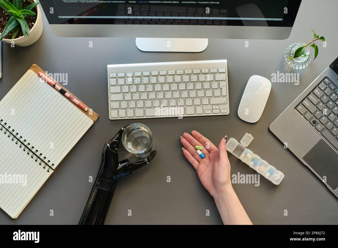 High angle view of woman with prosthetic arm taking medicine while working on computer at her workplace Stock Photo