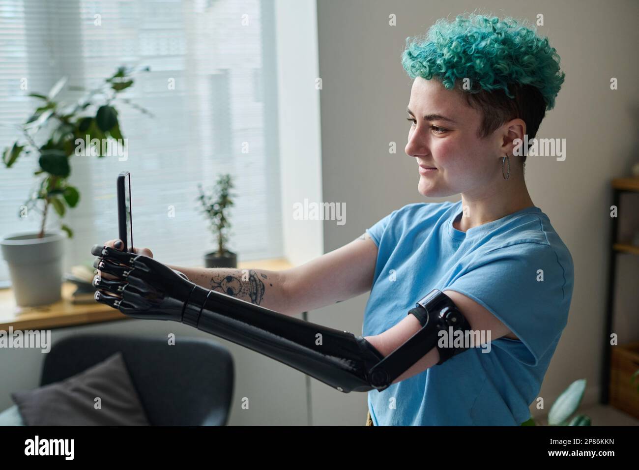 Young blogger with prosthetic arm using smartphone to talk to her followers during online broadcast Stock Photo