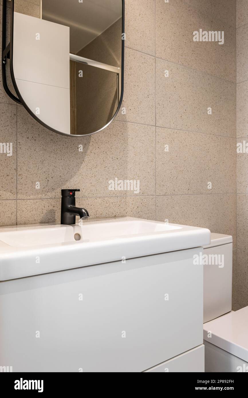 Fragment of mirror and sink with black faucet and toilet bowl in the bathroom on background of beige tiles. Concept of a simple but concise bathroom Stock Photo
