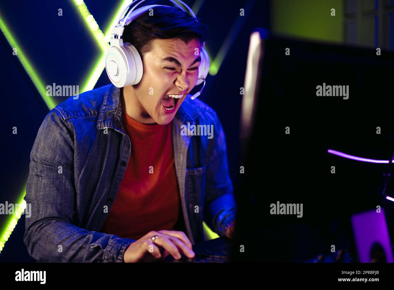 Gamer letting out a shout as he reaches a climactic point in his PC gaming session. With intense focus and determination on his face, he expresses thr Stock Photo