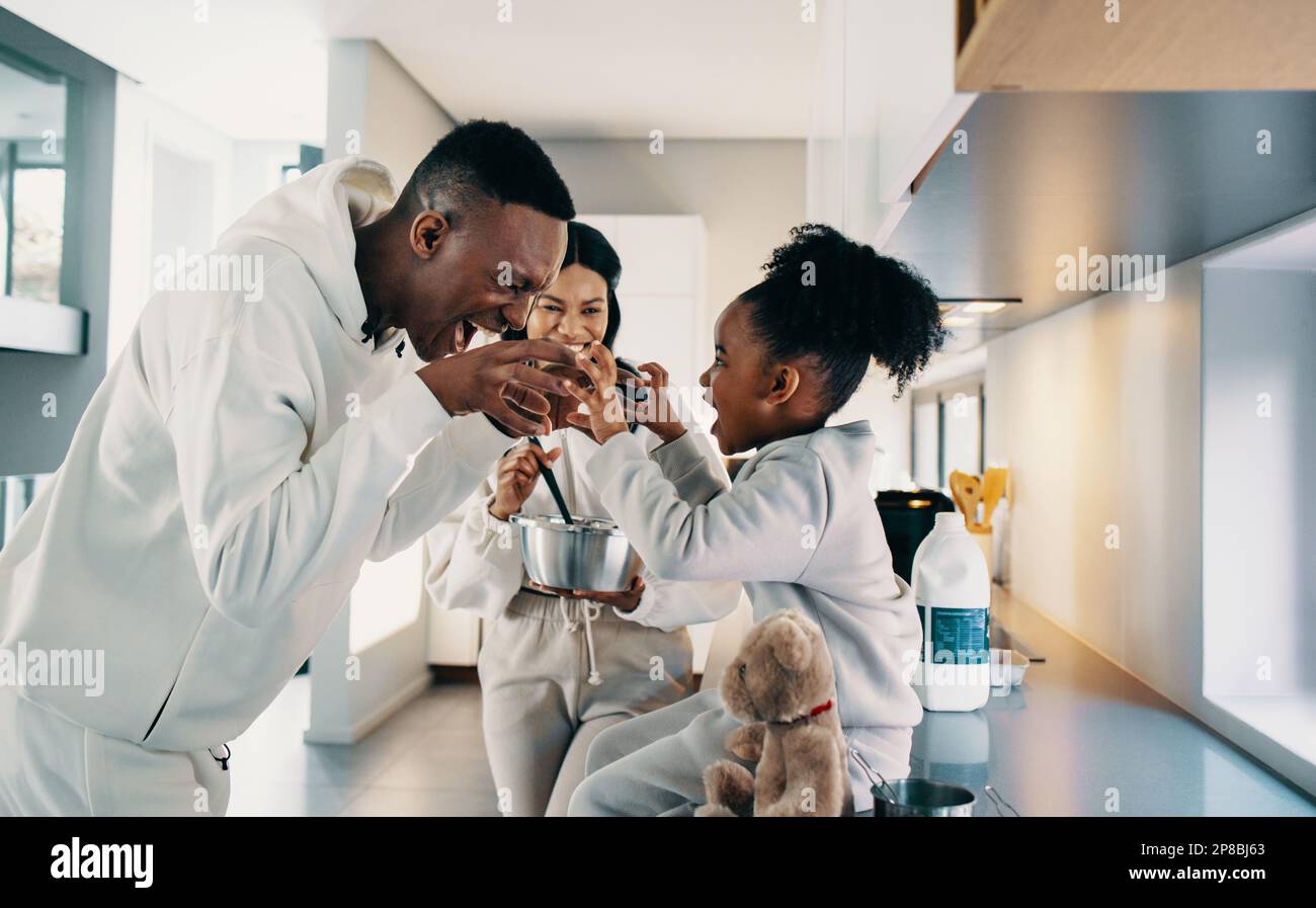 Dad and daughter playing a game together while mom makes breakfast in the kitchen. Father and daughter have a great relationship and mom is smiling. H Stock Photo