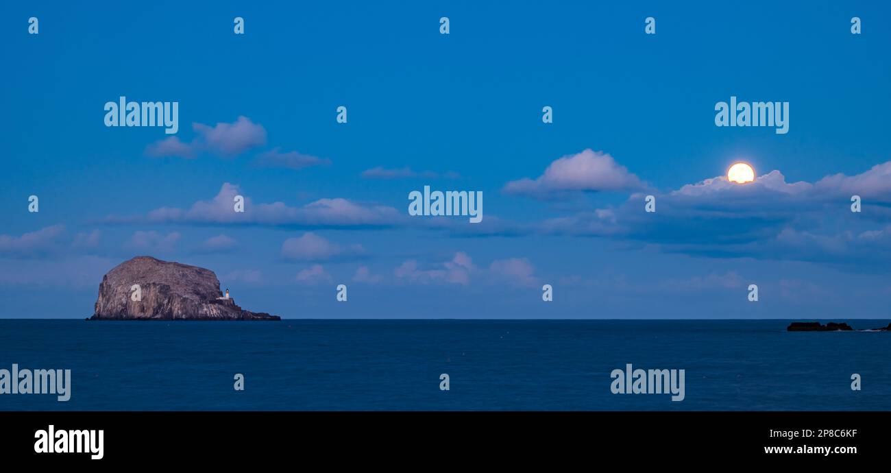 Bass Rock island at twilight with full moon rising behind clouds. Firth