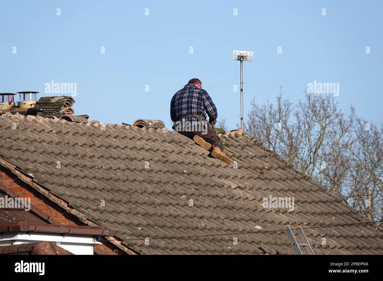 A roofer repairing ridge tiles on the roof of a domestic house Stock Photo
