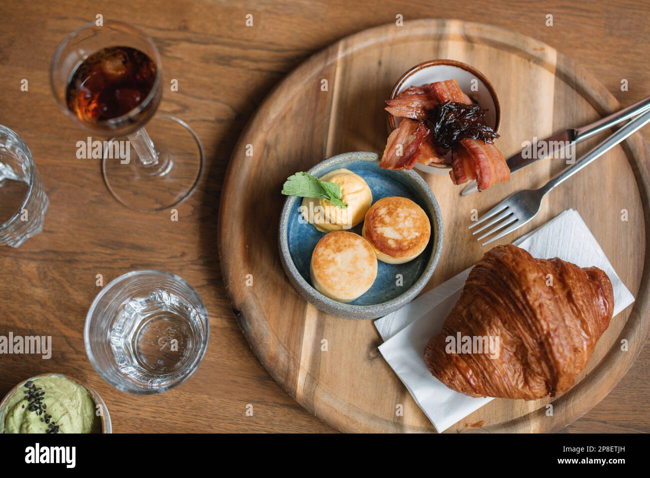 Overhead view of a brunch table with croissant, bacon, avocado, water