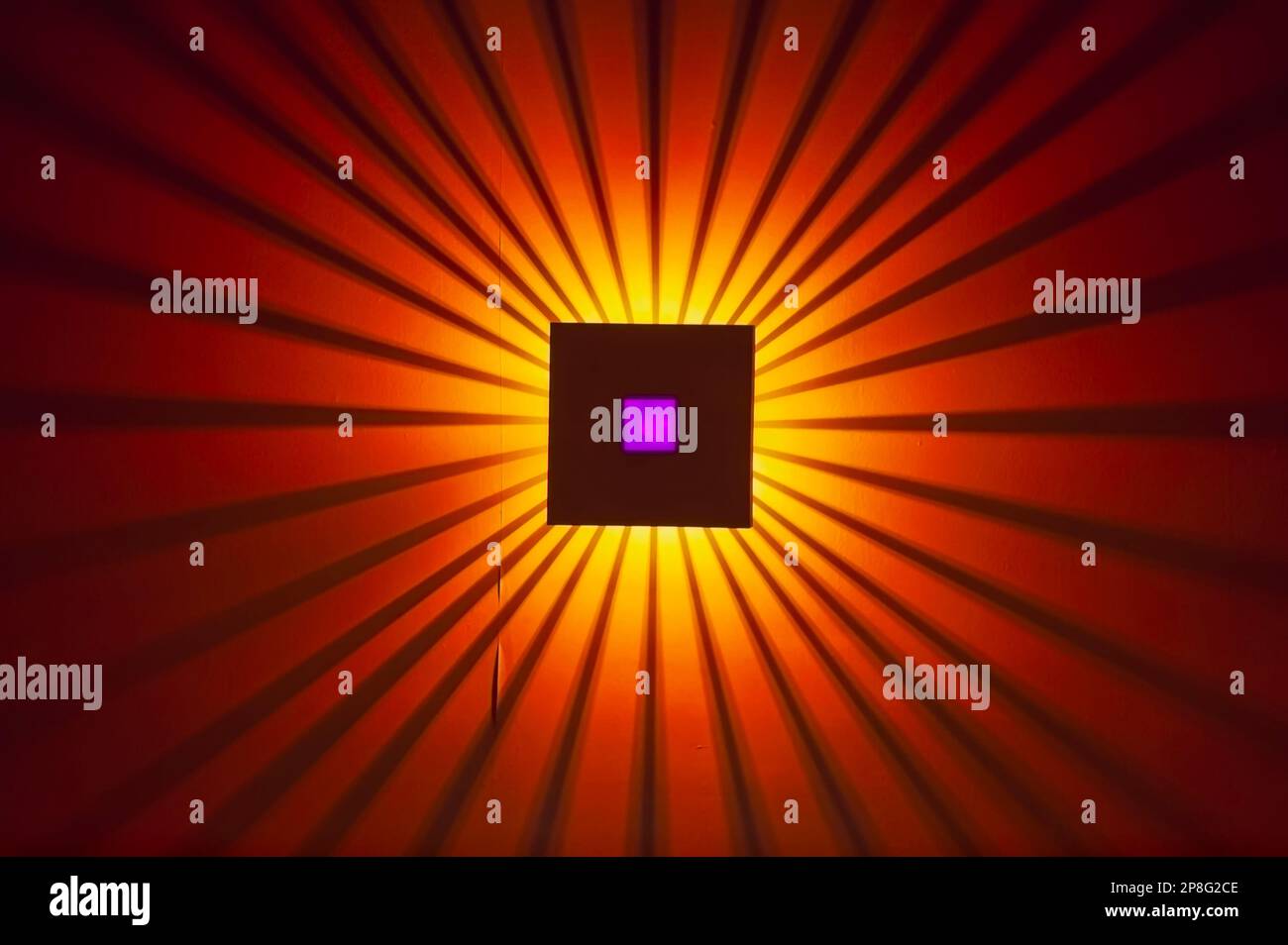A wall light glowing in the dark and casting a sunburst or a starburst
