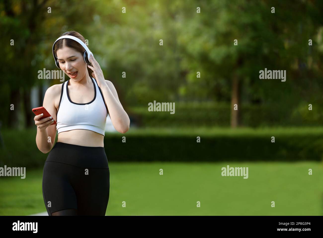 Young woman in sportswear listening to music with headphones and using smartphone after exercising on city streets. Stock Photo