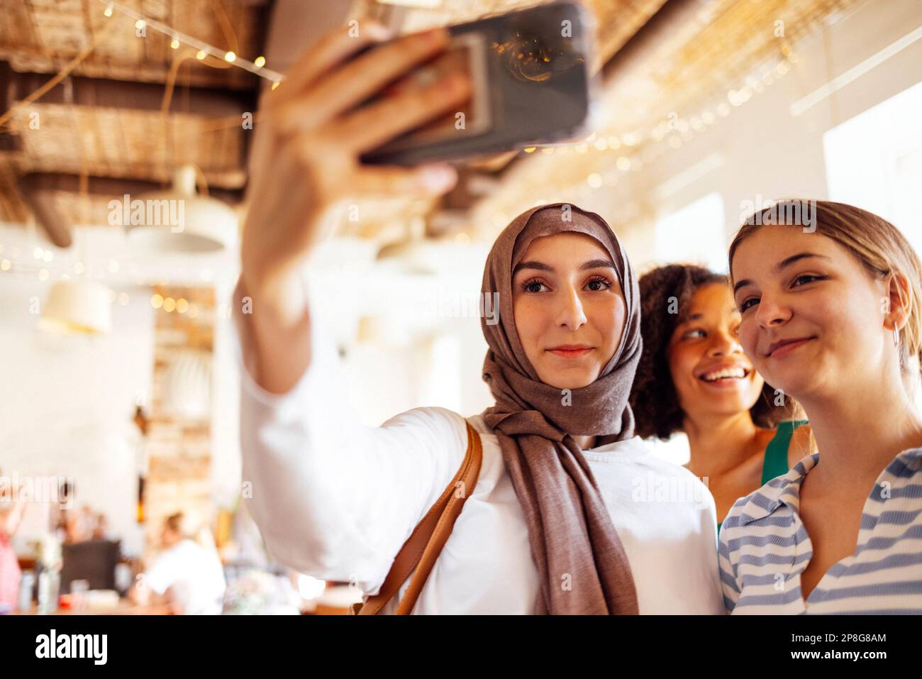 Three cute teen girls of different nationalities taking a selfie. Caucasian, afro american and muslim female teenagers takes a picture of theyself on Stock Photo