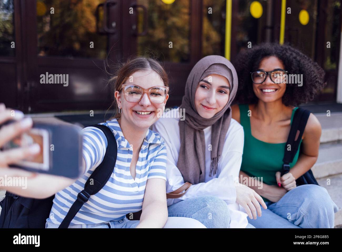 Three cute teen girls of different nationalities taking a selfie. Caucasian, afro american and muslim female teenagers takes a picture of theyself on Stock Photo