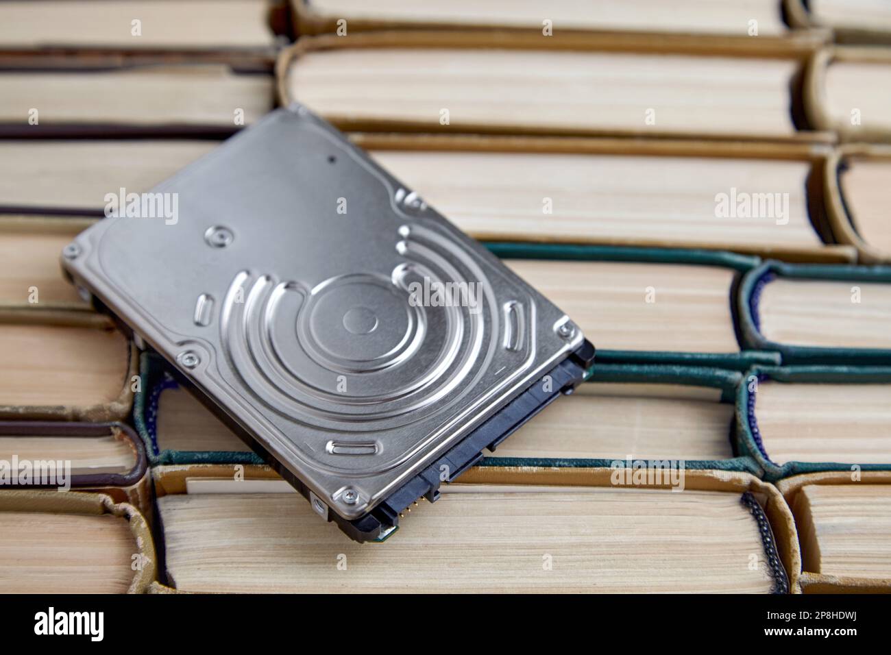 The hard drive of the computer lies on a pile of shabby paper books. Carriers of information from different eras. Stock Photo