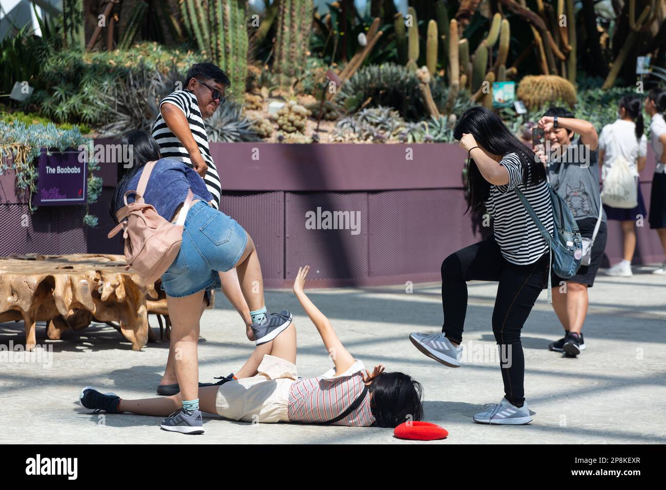 Weird family, the mother is taking group photo of family members to step their daughter on the floor in public space, they are just playing. Stock Photo