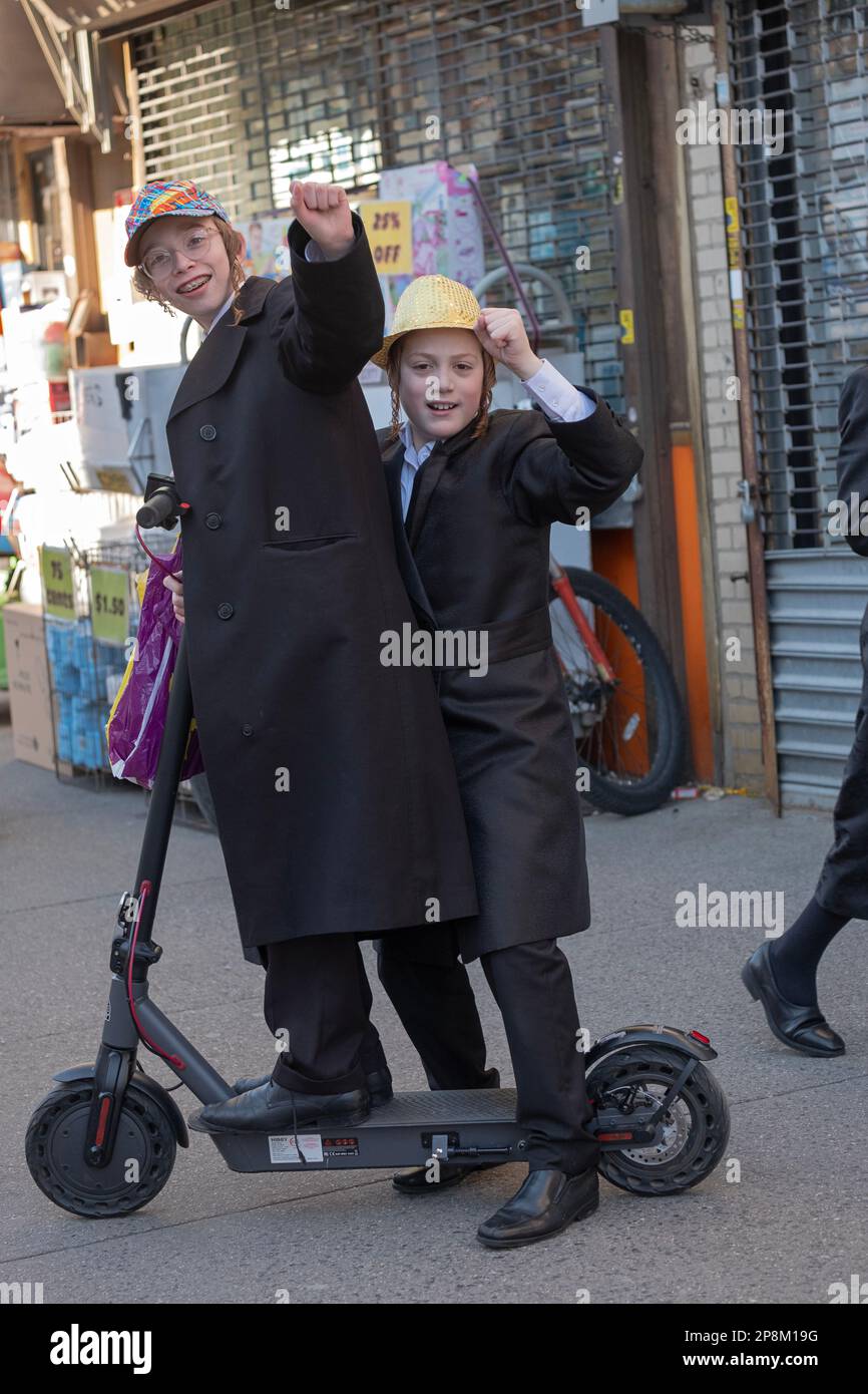 Two orthodox Jewish teenagers display Purim joy while sharing a ride on a scooter. On Lee Avenue in Williamsburg, Brooklyn, New York. Stock Photo