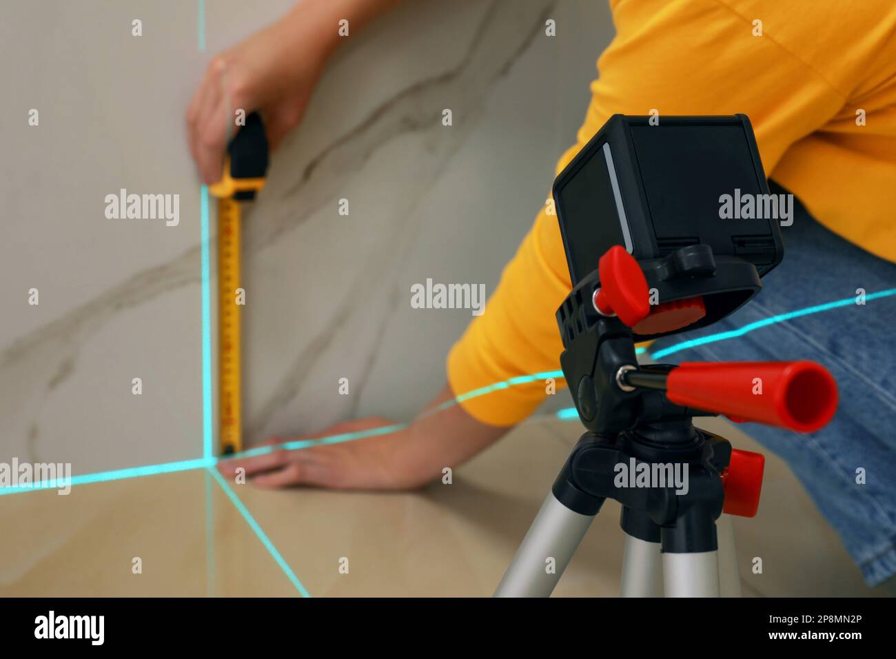 Woman using cross line laser level and tape for accurate measurement on ...