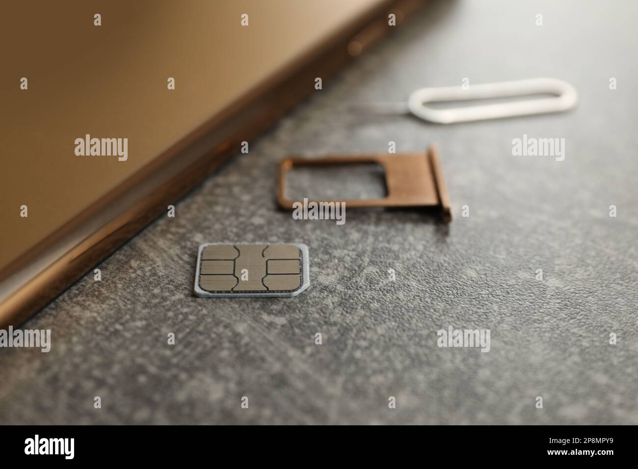 SIM card, mobile phone, tray and ejector tool on grey table, closeup Stock Photo