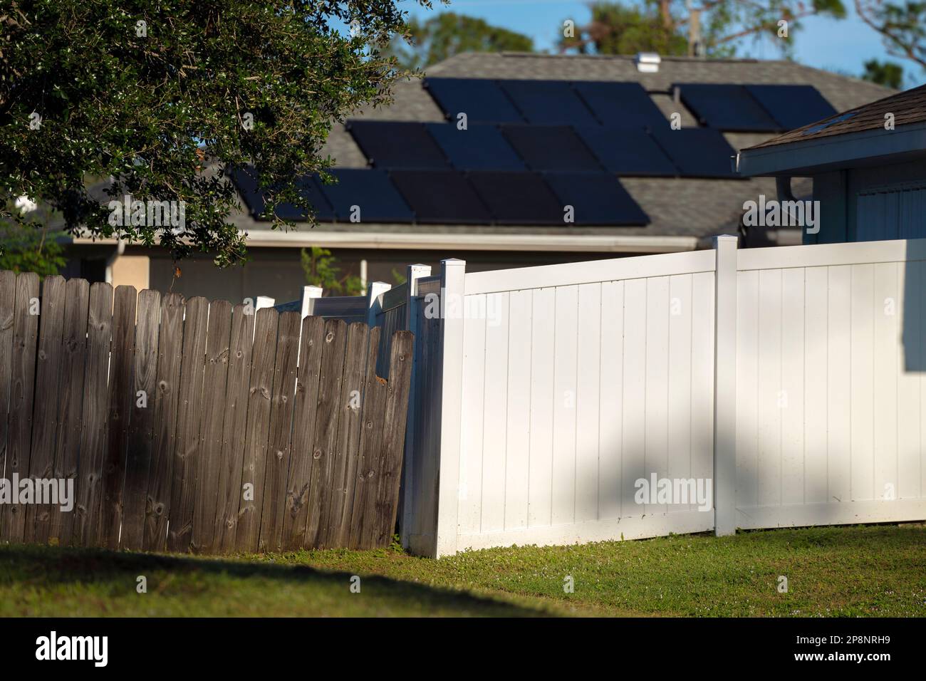 White vinyl picket fence on green lawn surrounding property grounds for backyard protection and privacy. Stock Photo