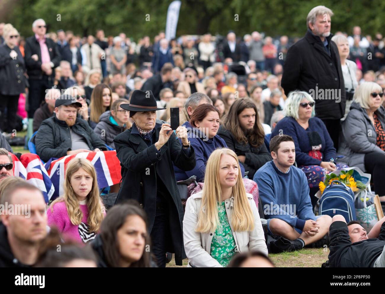 People watch the TV coverage of the late Queen Elizabeth II’s funeral day on a large screen in Hyde Park, London. Stock Photo