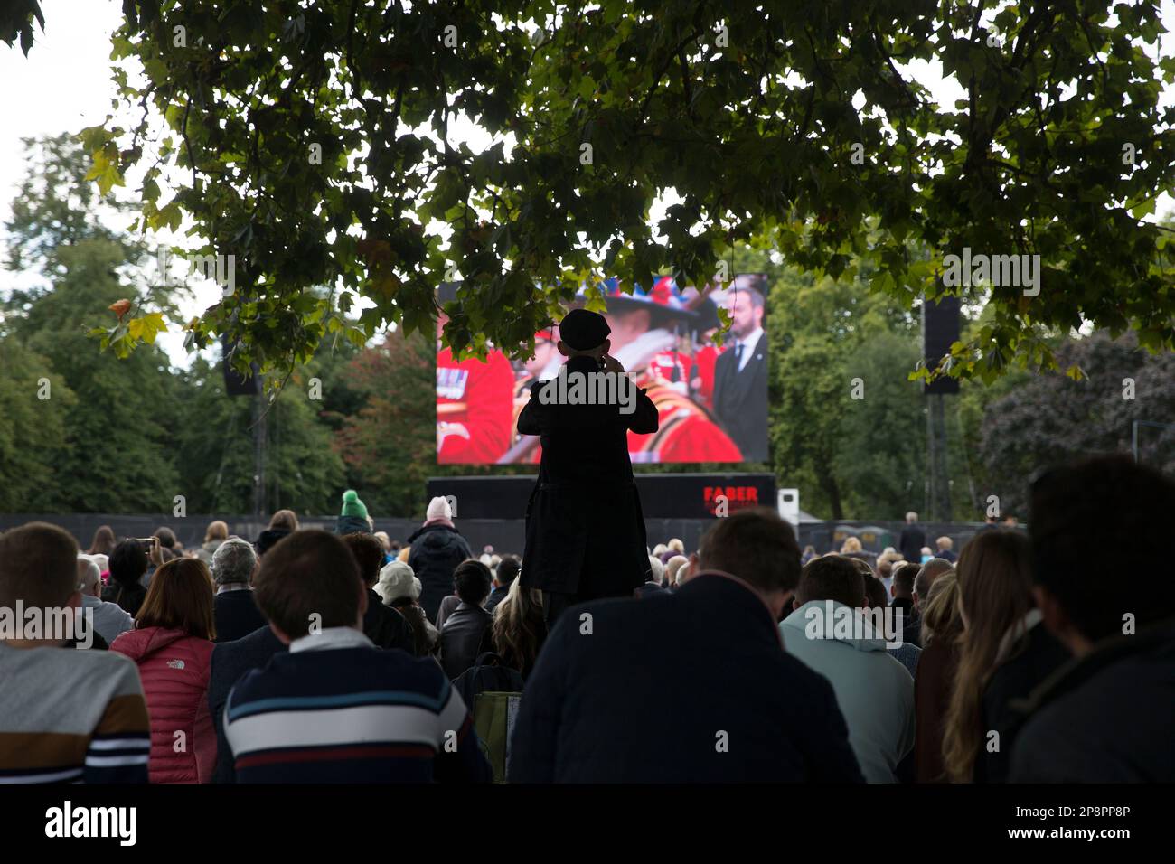 People watch the TV coverage of the late Queen Elizabeth II’s funeral day on a large screen in Hyde Park, London. Stock Photo