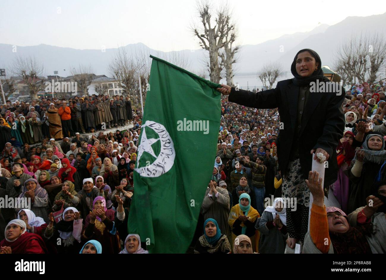 A Kashmiri Muslim woman holds an Islamic flag while others raise their ...