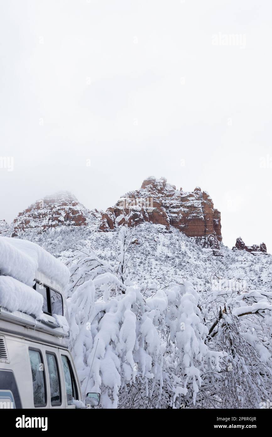 A camper van covered in deep snow, with snowy red rock mountains in the ...