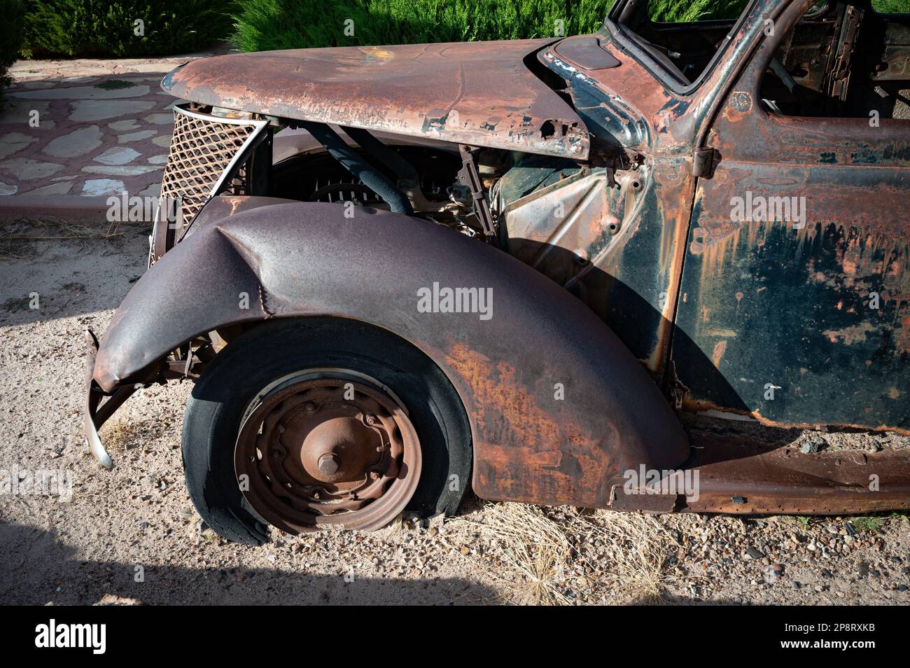 An old, rusted car sitting in a gravel parking lot, its paint job faded