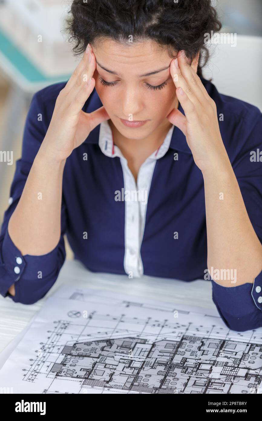 tired female architect looking at blueprint Stock Photo - Alamy