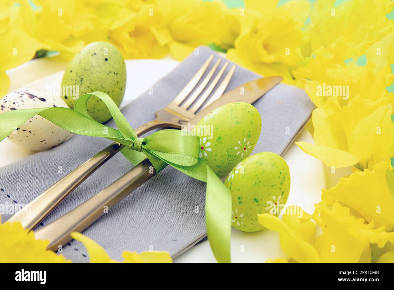 Easter table setting, Yellow Spring flowers and eggs decoration, napkin and golden cutlery on white plates, close up view Stock Photo