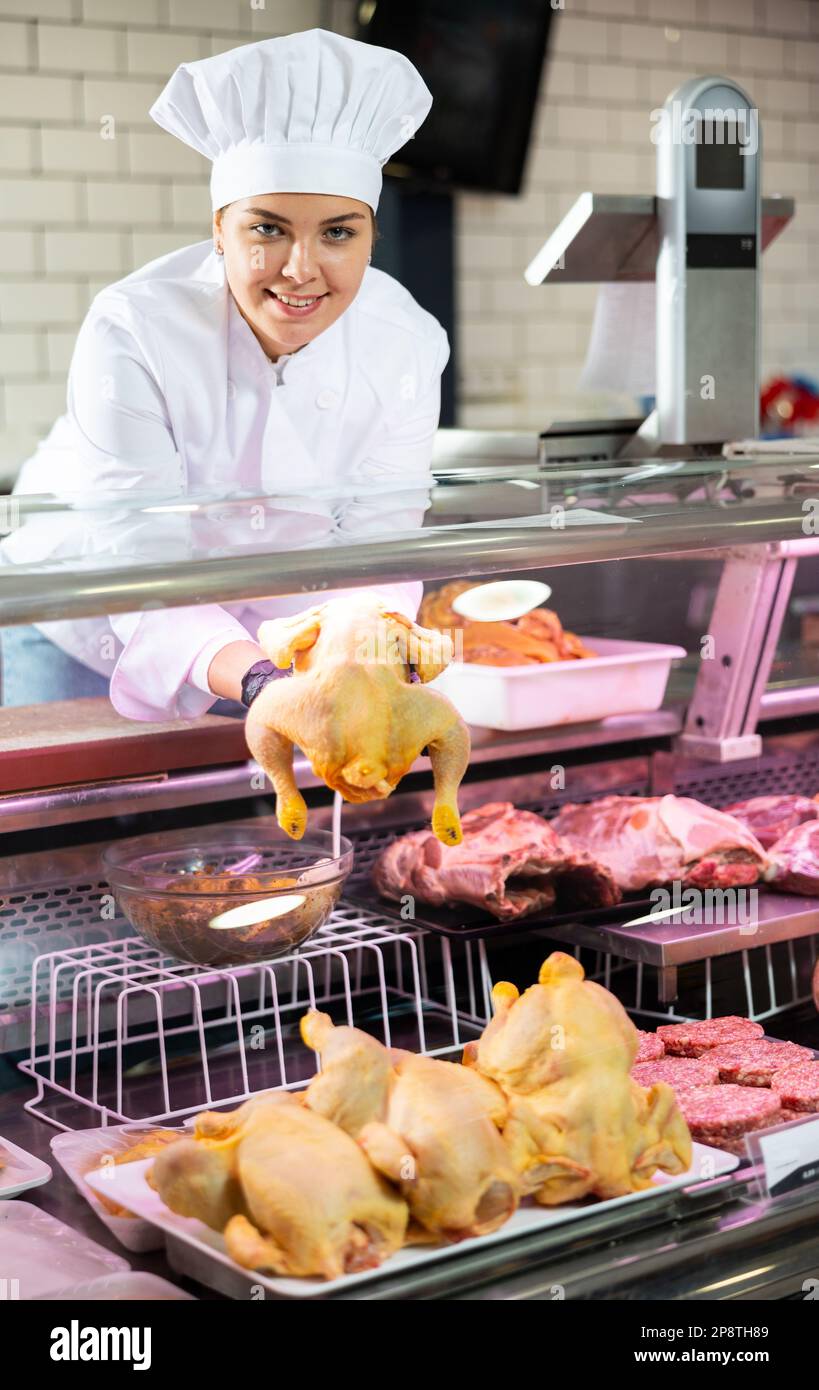 Young female butcher showing fresh whole chicken in butchery Stock Photo