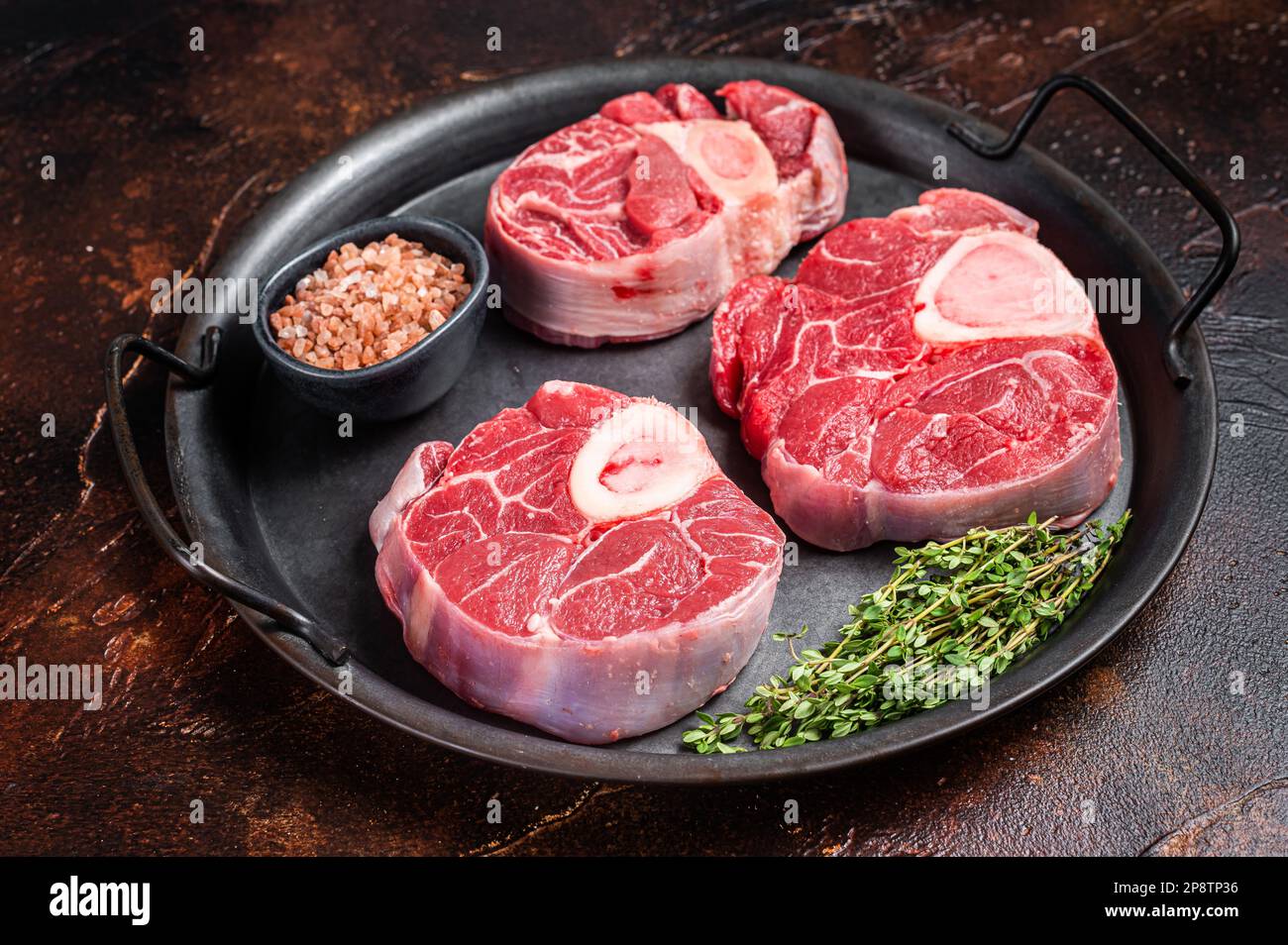 Raw Osso buco Veal shank steak, meat Ossobuco in steel tray. Dark background. Top view. Stock Photo