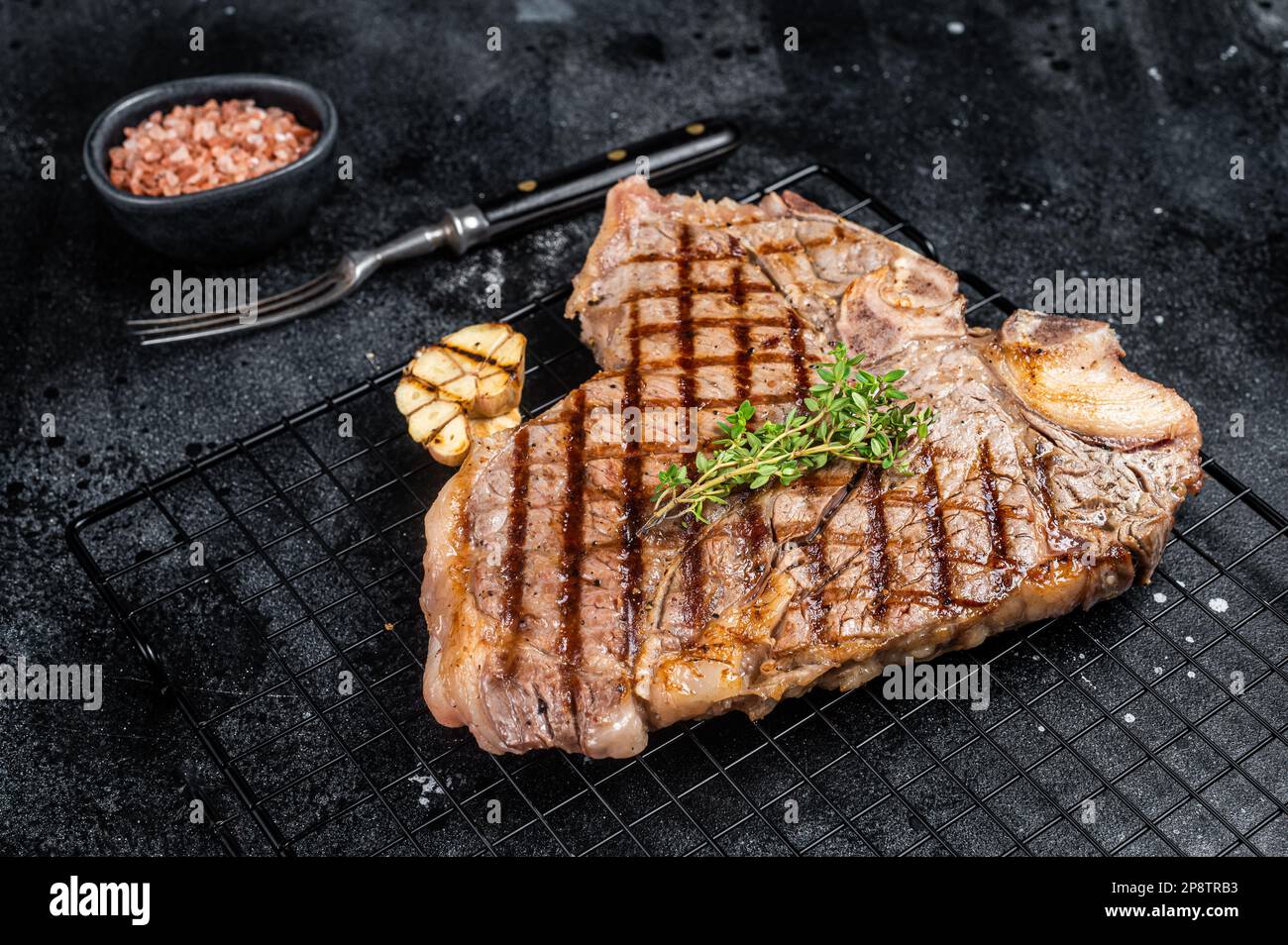 Grilled T-bone or Porterhouse beef meat Steak on a rack. Black background. Top view. Stock Photo