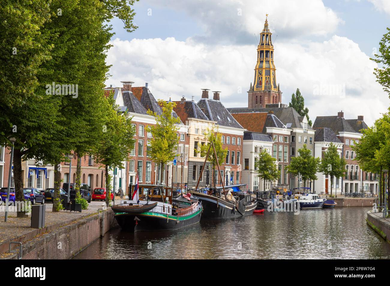 Historic ships, canal houses and warehouses on the old harbor at the Hoge der A with the tower of the historic Der Aa church in Groningen. Stock Photo