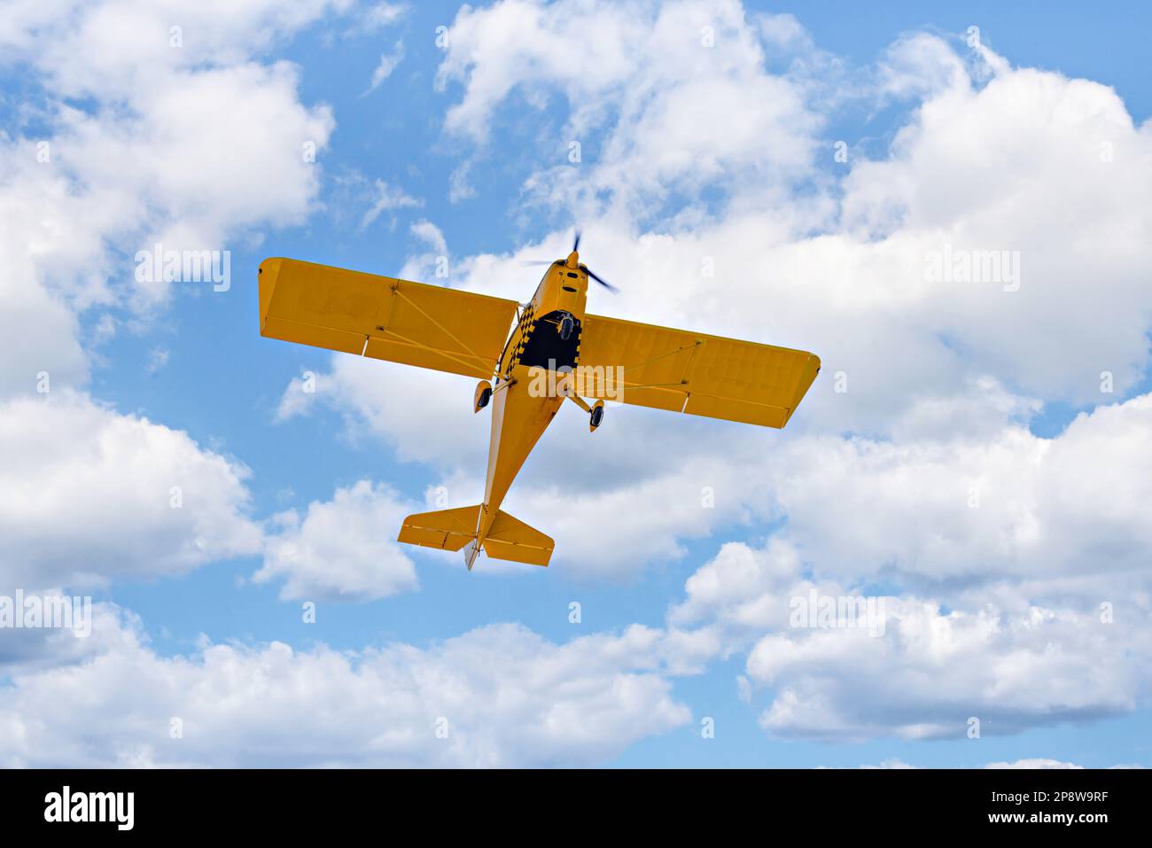 Yellow single-engine ultralight airplane flying in the blue sky with white clouds Stock Photo
