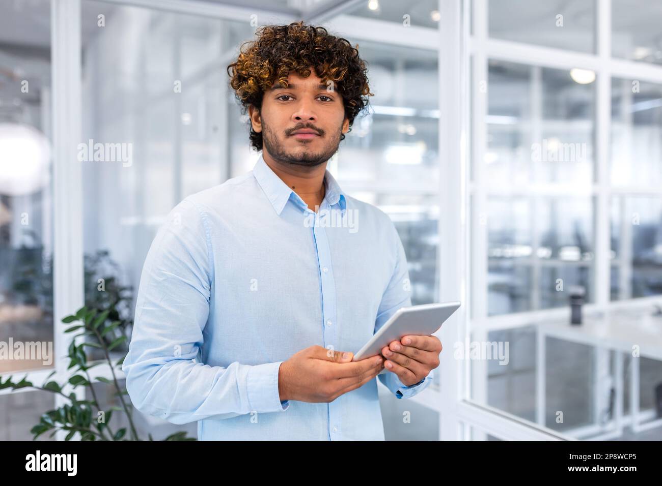 Portrait of a young Hispanic male student in a blue shirt standing in ...