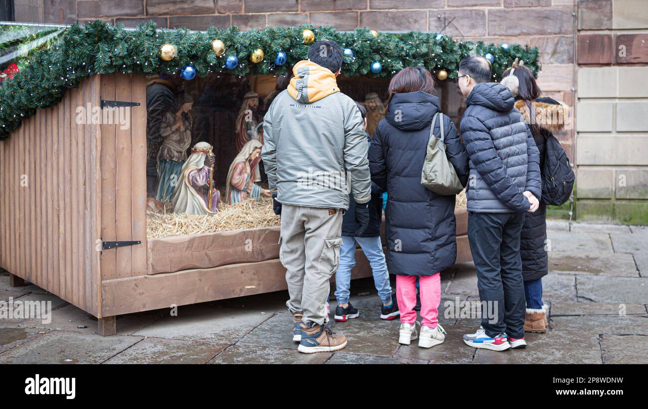 Manchester UK A group of people stand looking at the Nativity set in a wooden hut at St. Annes Square Stock Photo