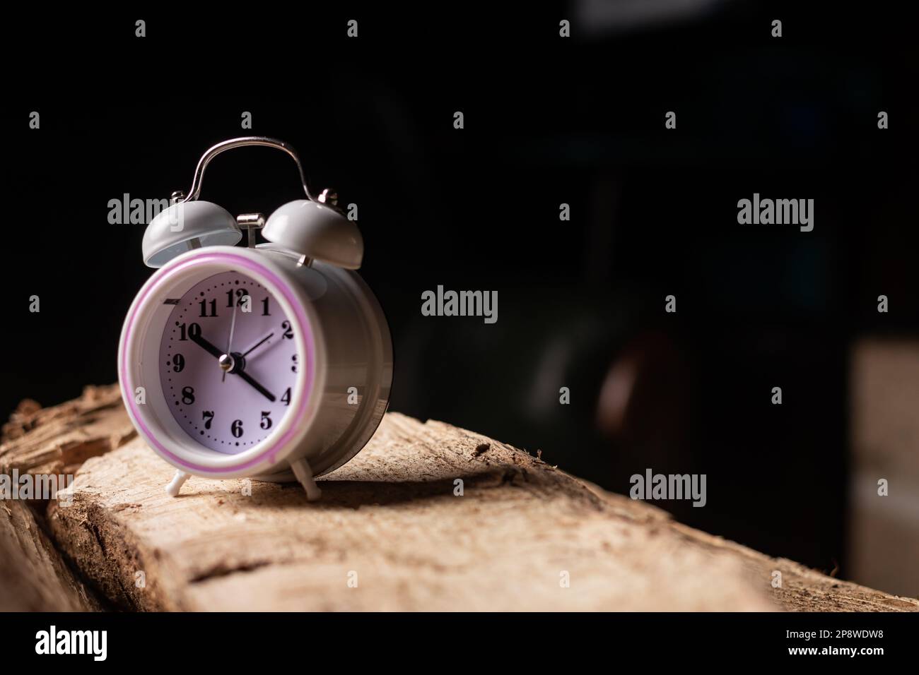 Alarm clock on log on dark background. Concept of time management
