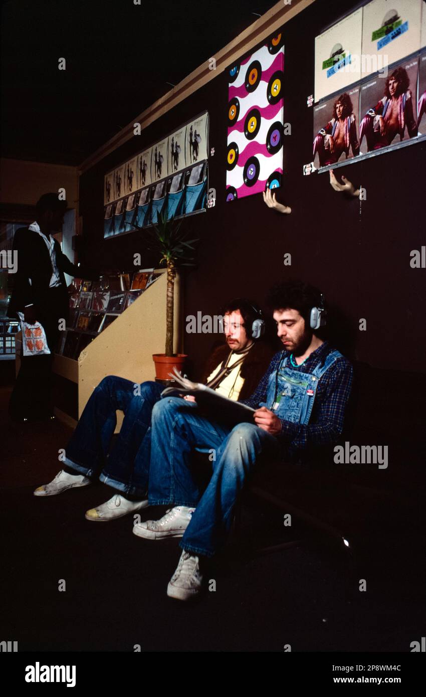 UK, London. 1977. Listening to vinyl records on headphones in a record shop. Latest releases covers on the wall including Fleetwood Mac - Rumours, Peter Gabriel - his first solo album and Peter Frampton -  I'm in You. Stock Photo